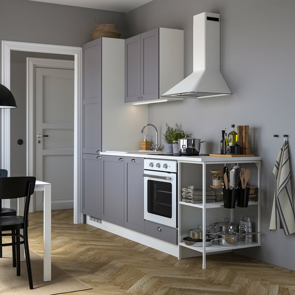 Modern gray kitchen with ENHET cabinets, white appliances, wooden floor, black chair, and plants.