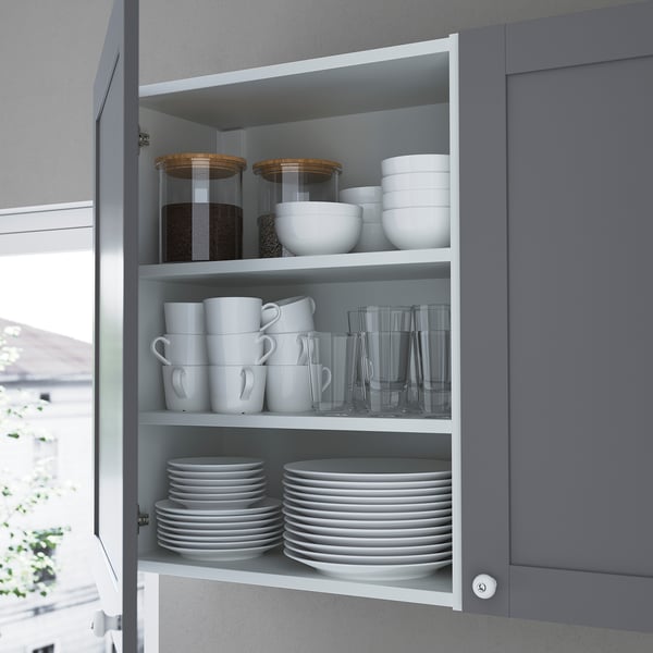 Open grey kitchen cabinet displaying organized dishes, cups, bowls, and jars with ample storage.