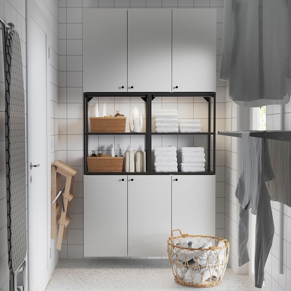 Modern bathroom with ENHET white cabinet and black frame. Its larger than the basket and ironing board, storing towels and supplies neatly.