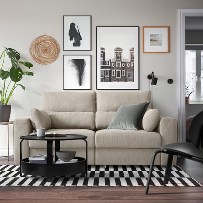 Modern living room with beige sofa, pillows, black coffee table, and wall art. Spacious and relaxing.