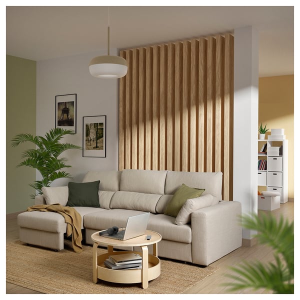 Modern living room with beige ESKILSTUNA sofa, wooden divider, white coffee table, plants, cozy pillows, and space divider.