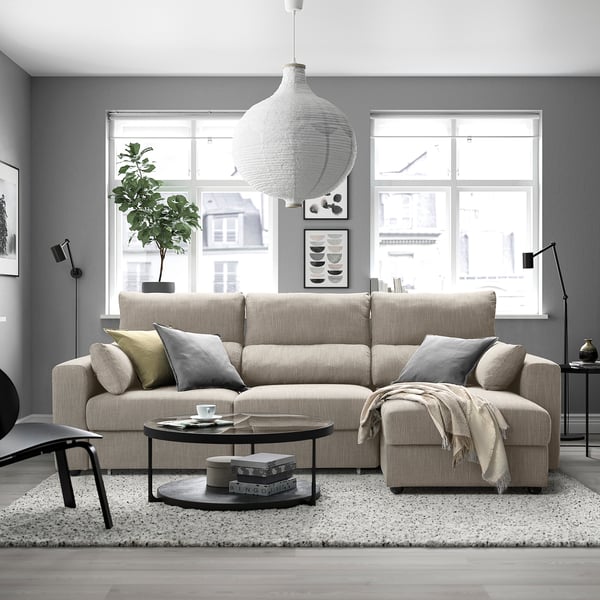 Modern living room with beige ESKILSTUNA sofa, coffee table, rug, plant, art, urban view.