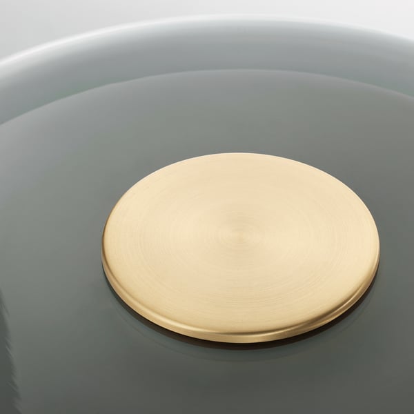 A brass-colored, circular lamp lid in a rounded bowl. The lid sits centered, reflecting light with a smooth, polished finish.