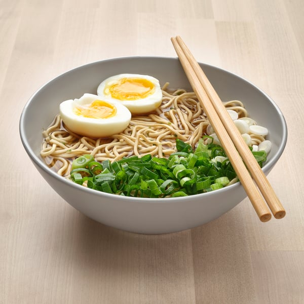 A bowl of noodles and vegetables with chopsticks.