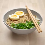 A bowl of noodles and vegetables with chopsticks.