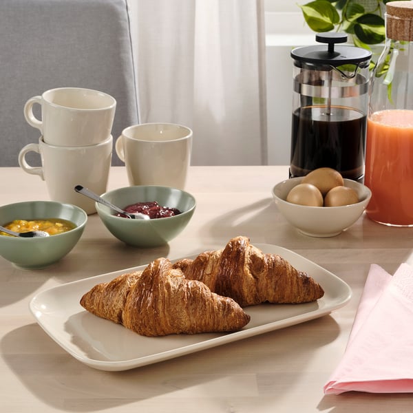 Table set with FÄRGKLAR plate, cups, bowls, and french press. Accompanied by croissants, jam, and orange juice.