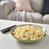 Bowl of popcorn and tv remote on a coffee table, suggesting a relaxed movie night at home.