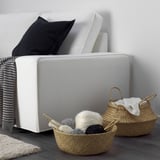 A white sofa with woven baskets underneath holding yarn and knitting needles.