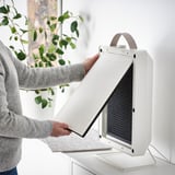 Person places air filter in air purifier; remove, install to clean air, trap particles like dust, pollen.