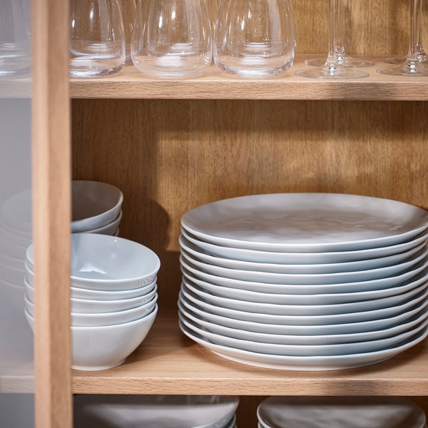 Wooden shelf with stacks of white porcelain plates, bowls, and clear wine glasses.
