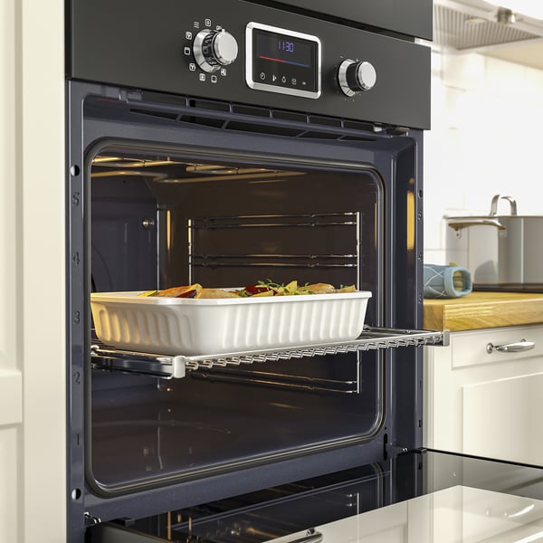 Black oven with digital display baking casserole; touch controls and telescopic rails visible.