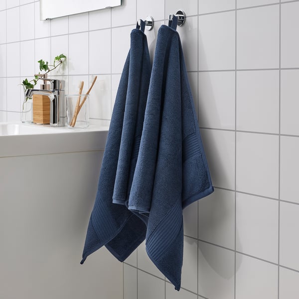 Two navy blue FREDRIKSJÖN towels on silver hooks, displayed prominently against white tiles, with clear containers and a plant nearby.