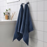 Two navy blue FREDRIKSJÖN towels on silver hooks, displayed prominently against white tiles, with clear containers and a plant nearby.
