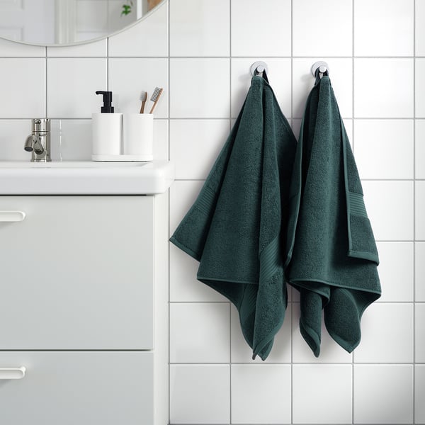 FREDRIKSJÖN dark green towels hang neatly near sink, showcasing their thick, 100% cotton texture and elegant woven border, larger than nearby items.