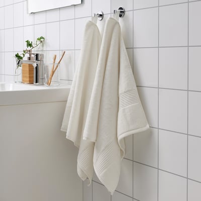White FREDRIKSJÖN towels hang neatly, thicker with woven borders, plus smaller items on a shelf, crisp white bathroom setting.