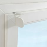 White drill-free bracket mounted on a window frame, holding a roller blind, showcasing easy and removable window treatment installation.
