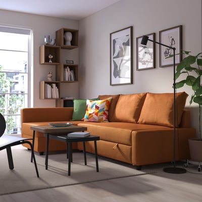Bright orange FRIHETEN sofa-bed in modern living room. Its large, matching other furnishings, with colorful pillows and art on walls.