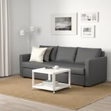 Modern living room with FRIHETEN sofa bed, white coffee table, and black-and-white photos.
