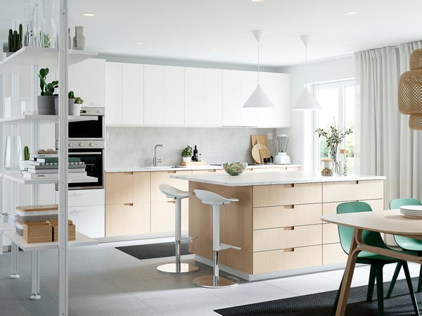 Modern, bright kitchen with white & bamboo cabinets, an island, white pendant lights, green & wooden chairs, plants, clean design.