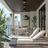 Modern outdoor lounge with white cushioned chairs, dining table, and glass railings. Plants and grey blanket add to cozy, minimalist design.