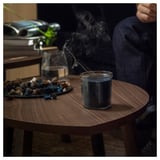 Dim room: FRUKTSKOG candle emits smoke on wooden table with stones and glass.