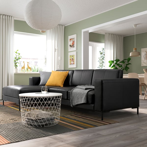 Modern living room with black FULLERÖ sectional, yellow pillow, white coffee table, green walls, striped floors, and large windows.