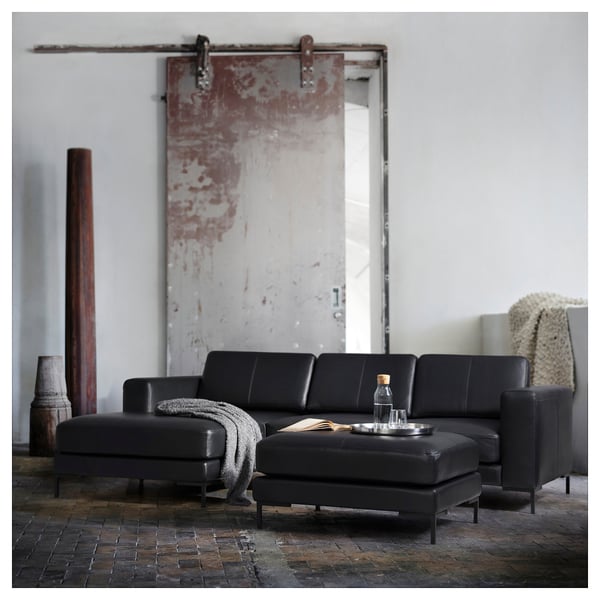 Modern living room with sleek black leather sectional sofa, wooden coffee table, and rustic sliding door.