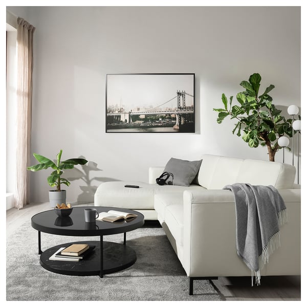 Cozy living room with white FULLERÖ sofa, round black coffee table, greenery, and cityscape artwork.