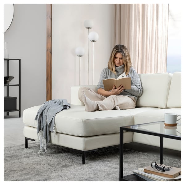 A woman reads on a white FULLERÖ sofa with a glass coffee table beside her.
