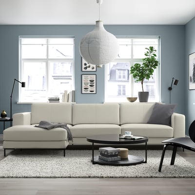 Modern living room with blue walls, featuring a large white sectional sofa, city view window, coffee table, and greenery.