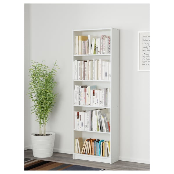 White bookcase with books, plant, and artwork.