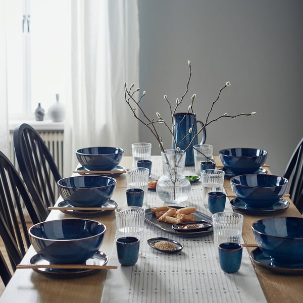 Table set with GLADELIG blue bowls, stoneware, deep & round, perfect for soups & pasta. Centered vase with branches.