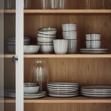 Wooden shelves with GLADELIG bowls, white with gray glaze, neatly stacked. Bowls vary in size, smaller ones nested inside larger ones.