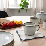 Breakfast table with GLADELIG mugs, cream jug, fruit, bread, plant.