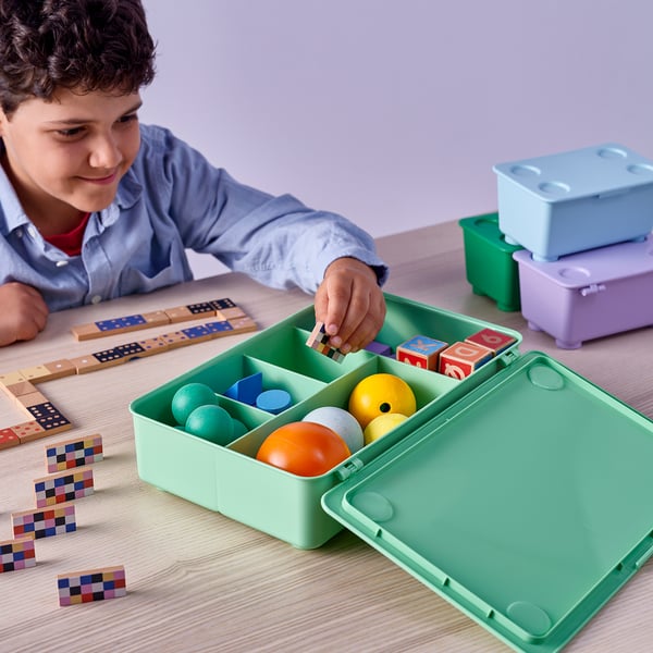Boy playing with blocks near a green GLIS box with toys inside.
