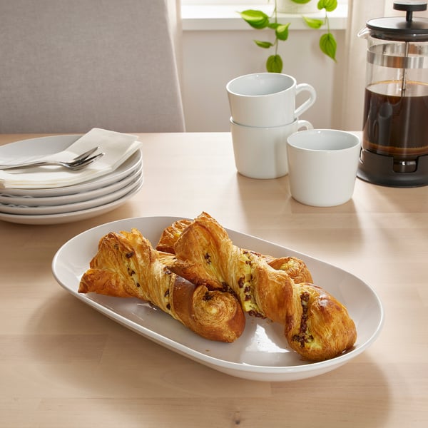 Golden-brown pastries on wood table with plates, mugs, and french press.