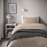 Cozy bed with beige duvet, gray blanket, wall light, & nightstand.