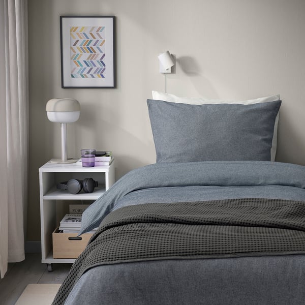 Modern bedroom with gray GROVSNÄRJA duvet set, white lamp, and headphones on nightstand.