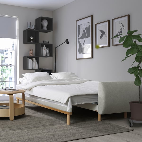 White sofa-bed in modern living room with plant, art, lamp, window & storage.