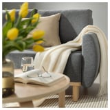 Cozy living room: gray sofa with throw, neutral pillows, yellow tulips, books, glass on table.