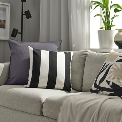 A GURLI grey cushion on a couch, surrounded by other cushions. The GURLI cushion is large, rectangular, and made of cotton.