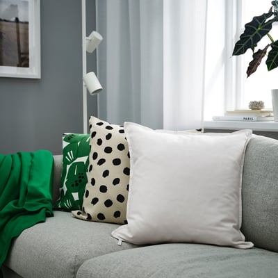 Modern living room with grey sofa, cushions, green blanket, plant, book, dark wall, frame.