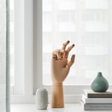 Wooden artist hand model near window with books and vases.