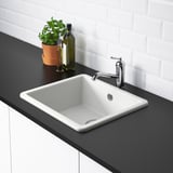 A minimalist kitchen sink with a chrome faucet set on a black countertop. The sink has rounded corners and is part of the HAVSEN series.