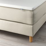 Close-up of IKEA bed with soft headboard, wooden legs, and washable mattress cover.