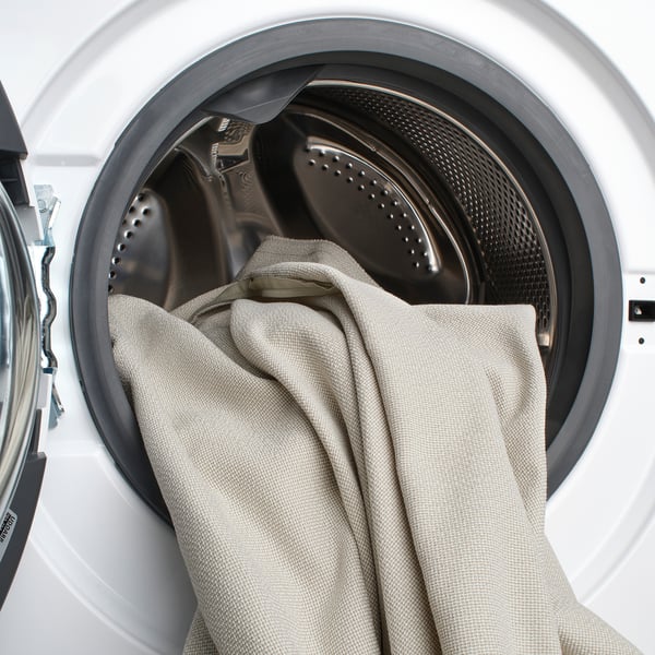 White washing machine with a light-colored bedsheet hanging partway out, illustrating its machine-washable feature.
