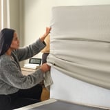 A woman adjusts soft, removable headboard of modern upholstered bed, showcasing comfort and easy cleaning.