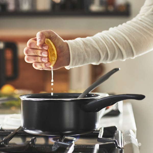 Squeezing lemon into a saucepan on a stove. The saucepan has a non-stick coating and is placed on a gas burner.