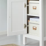 Open white wooden cabinet displaying three cream folders, one holding papers on middle shelf.