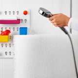 Person holding water sprayer, cleaning white mattress near colorful toys.